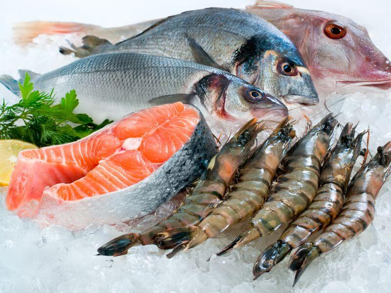 Whole fish, salmon fillets, and shrimp on crushed ice with lemon and parsley.