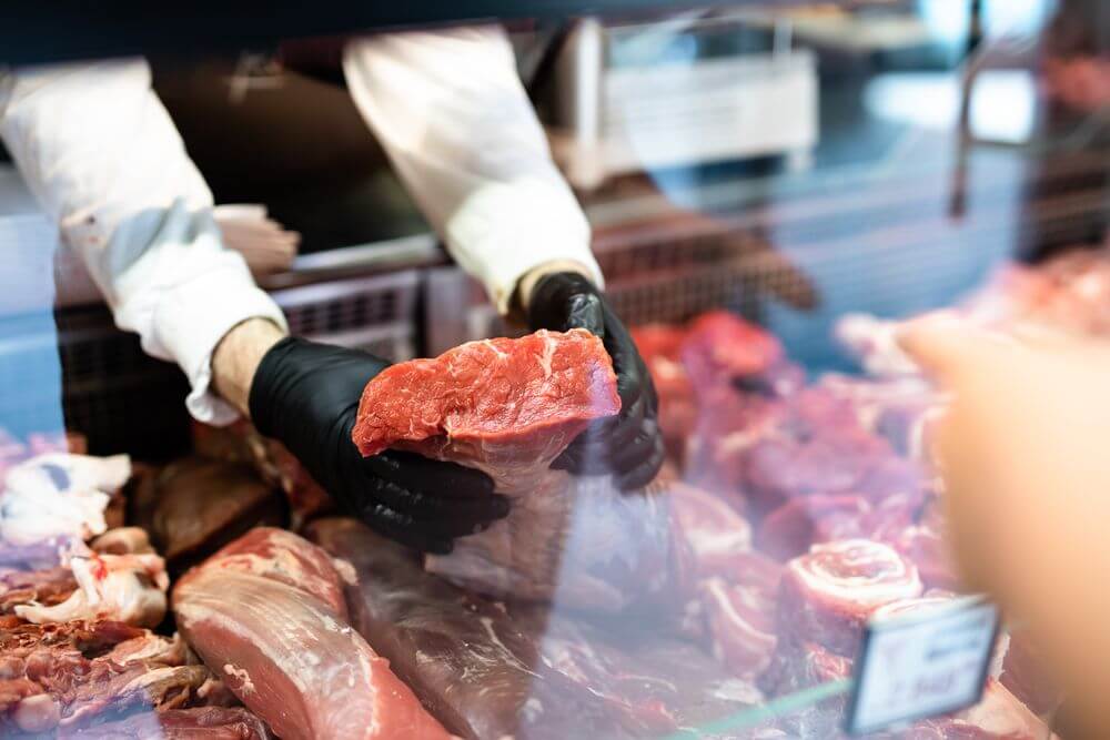 A butcher lifting a fresh cut of beef out of the display case.
